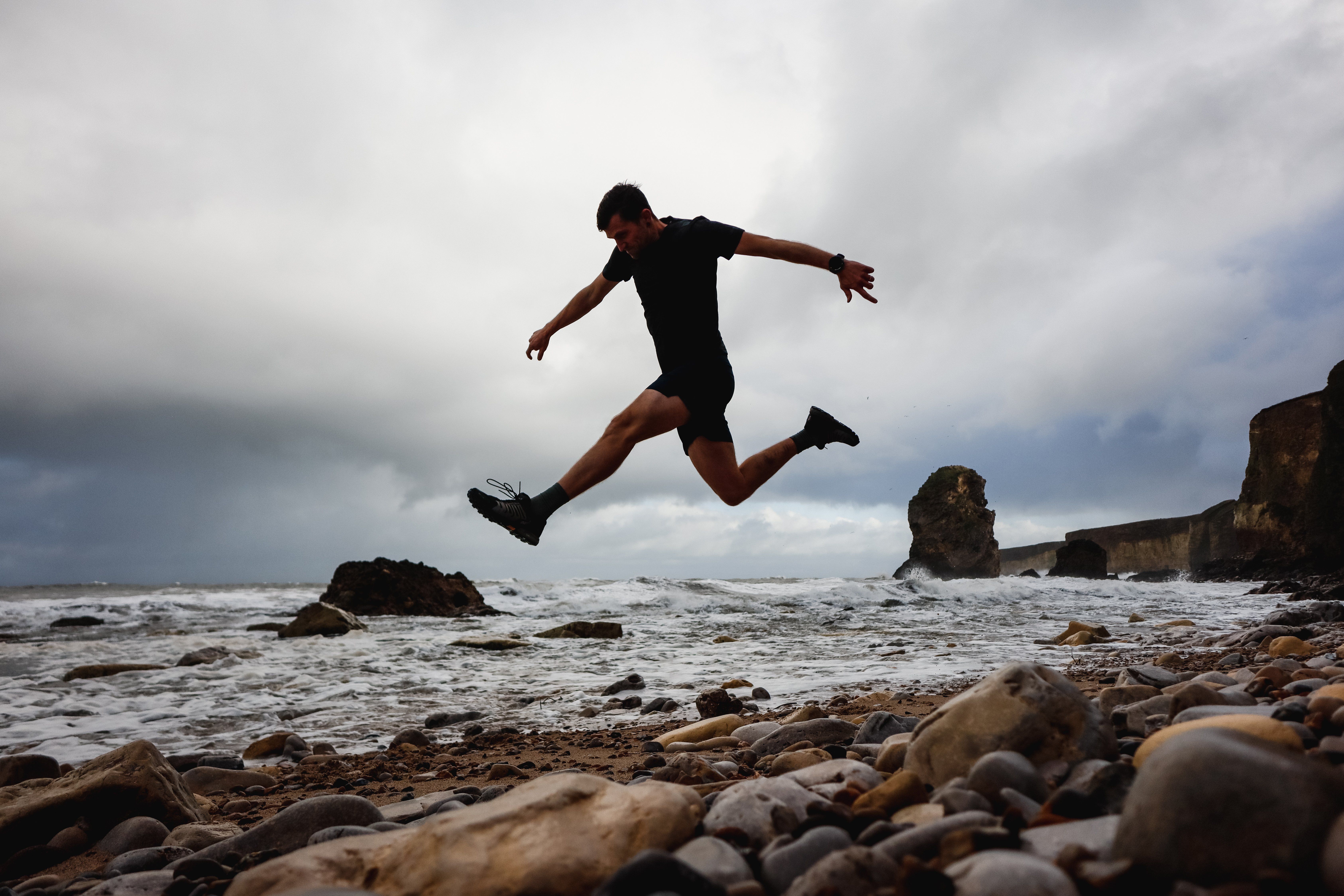 A trail runner captured jumping in the air on a rocky beach, creating a bold silhouette.